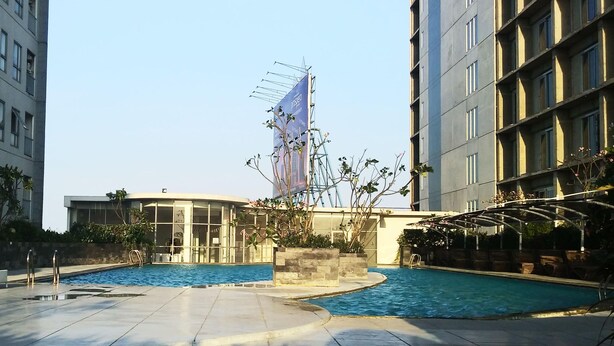 Un área de piscina con sillones de descanso, cielo despejado y un edificio con una gran bandera.