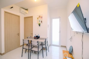 Um quarto com uma mesa de jantar, cadeiras, uma TV fixada na parede e uma porta.