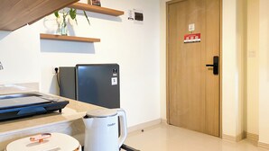 Una cocina moderna con refrigerador, hervidor de agua y cafetera. Se observa una puerta de madera y una repisa con una planta.