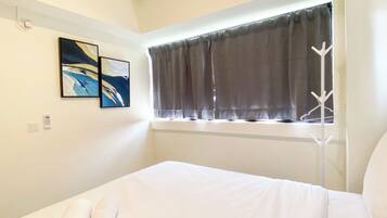 A hotel room with a bed, a window with curtains, a coat rack, and two paintings on the wall.
