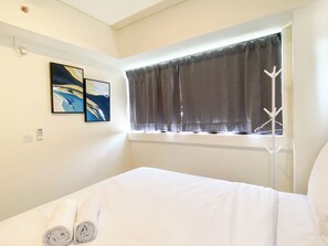 A hotel room with a bed, a window with curtains, a coat rack, and two paintings on the wall.