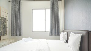 Ein Hotelzimmer mit zwei Betten, einem großen Fenster, grauen Vorhängen, einem Nachttisch und einem Kopfteil.