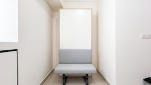 A narrow hallway with a grey bench, white walls, and a door with a wooden frame. - Enjoy Living Studio (No Kitchen) Bandaraya - Tallasa City Makassar Apartment (Makassar)