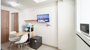 Eine moderne Küche mit Mikrowelle, kleinem Kühlschrank, einem Holztisch mit Stühlen und einem an der Wand montierten Fernseher, der eine Kindersendung zeigt.