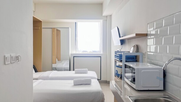 A hotel room with two beds, a small kitchenette, and a window with curtains. - Nice And Homey Studio (No Kitchen) At Bandaraya - Tallasa City Makassar Apartment (Makassar)