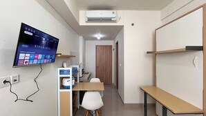 A compact room with a flat-screen TV mounted on the wall, a wooden door, a small table, and a white chair. - Nice And Homey Studio (No Kitchen) At Bandaraya - Tallasa City Makassar Apartment (Makassar)