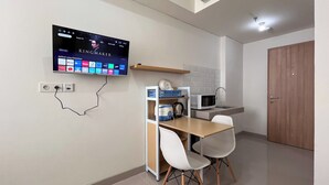 A small kitchenette with a microwave, a kettle, and a TV mounted on the wall displaying a movie. - Nice And Homey Studio (No Kitchen) At Bandaraya - Tallasa City Makassar Apartment (Makassar)