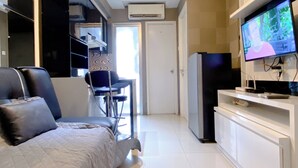 A modern living room with a sofa, a dining area with chairs, a television, and a refrigerator.