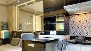 A compact hotel room with a kitchenette, a bed with a white duvet, a small desk, and a chair.