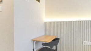 Ein kleiner, privater Arbeitsbereich mit einem Holztisch, einem schwarzen Stuhl, einem weißen Heizkörper und einer wandmontierten Steckdose.