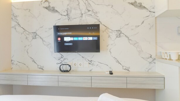 Ein modernes Hotelzimmer mit Marmorwand, einem an der Wand montierten Flachbildfernseher, einem Nachttisch mit Fernbedienung und einem Bett mit weißer Bettdecke.