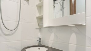 Ein Badezimmer mit schwarzem Waschbecken, weiß gefliesten Wänden und einer Dusche mit Glastür.
