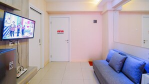 Una habitación de hotel moderna con una televisión de pantalla plana, un sofá gris y una puerta blanca con una etiqueta de detector de incendios.