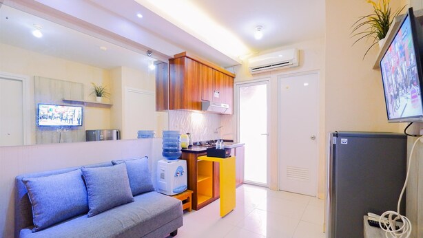 Un espacio habitable compacto con sofá, una pequeña zona de cocina, refrigerador y televisor montado en la pared.