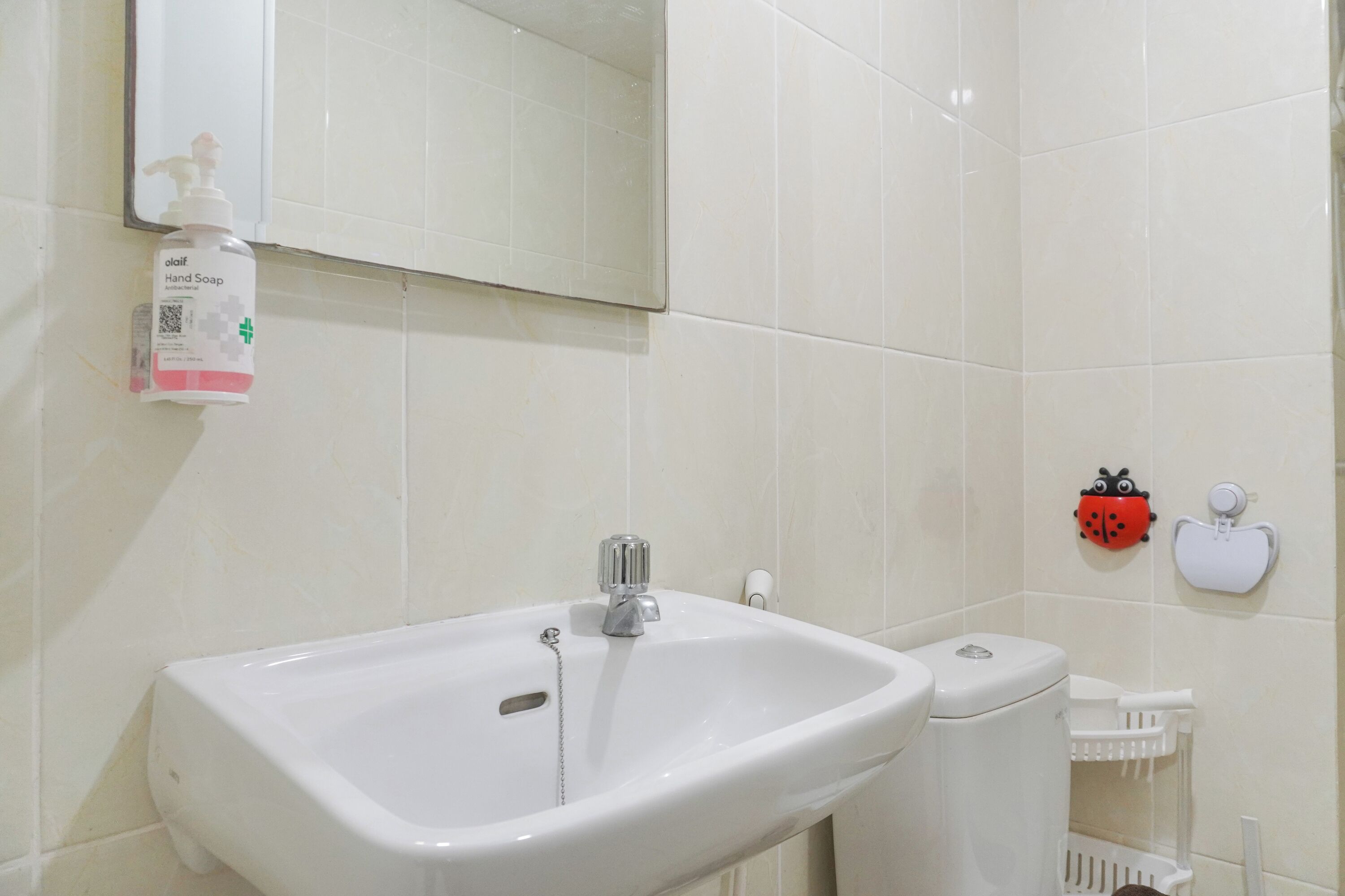 A bathroom with a white sink, a mirror, a toilet, and a hand soap dispenser.