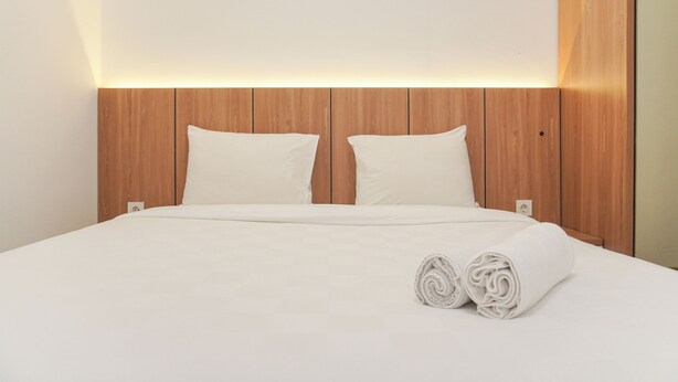 A neatly made bed with white linens and pillows, a wooden headboard, and a rolled towel on the bed.