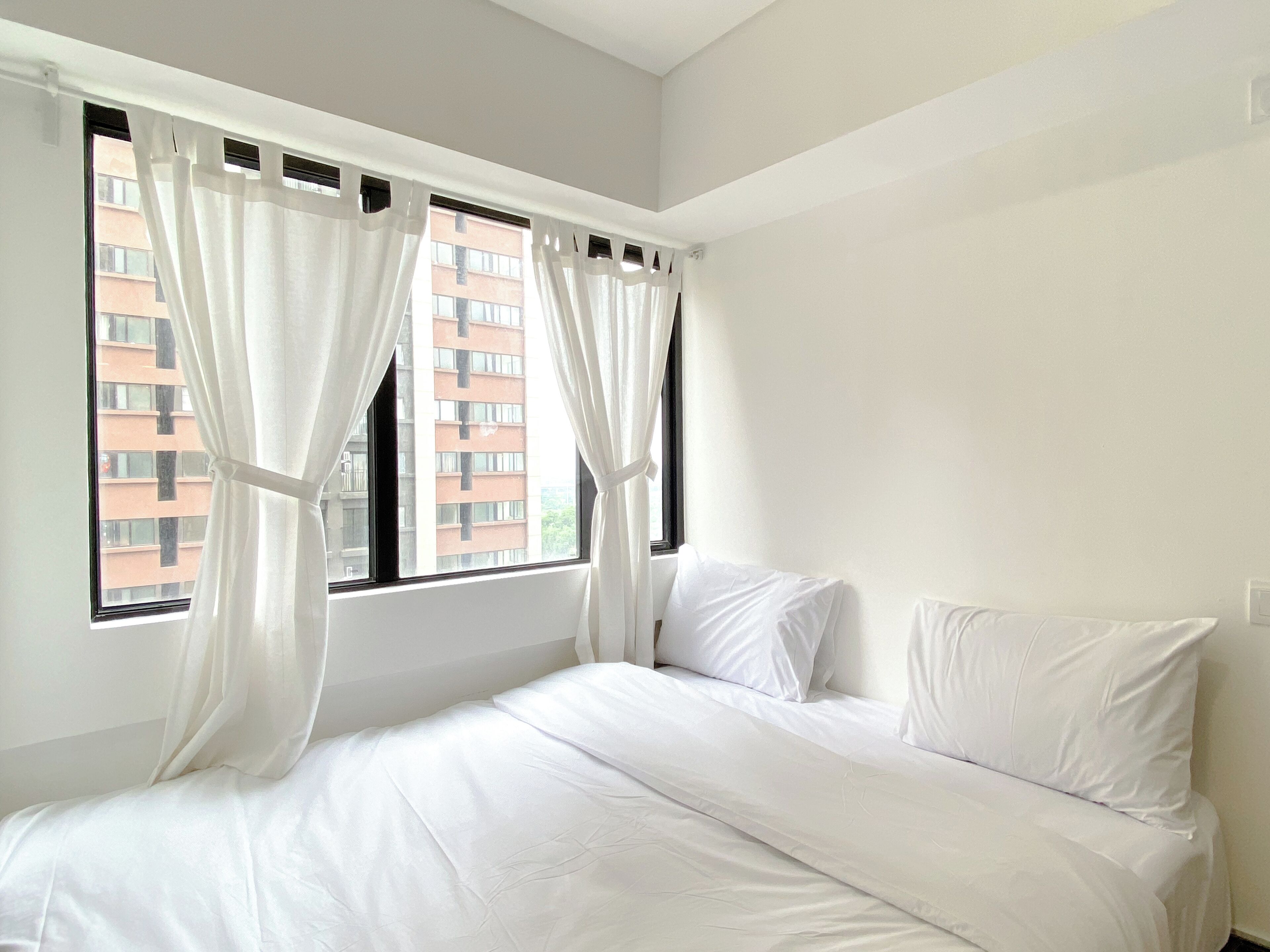 A bedroom with a bed, white curtains, and a view of a building through the window.