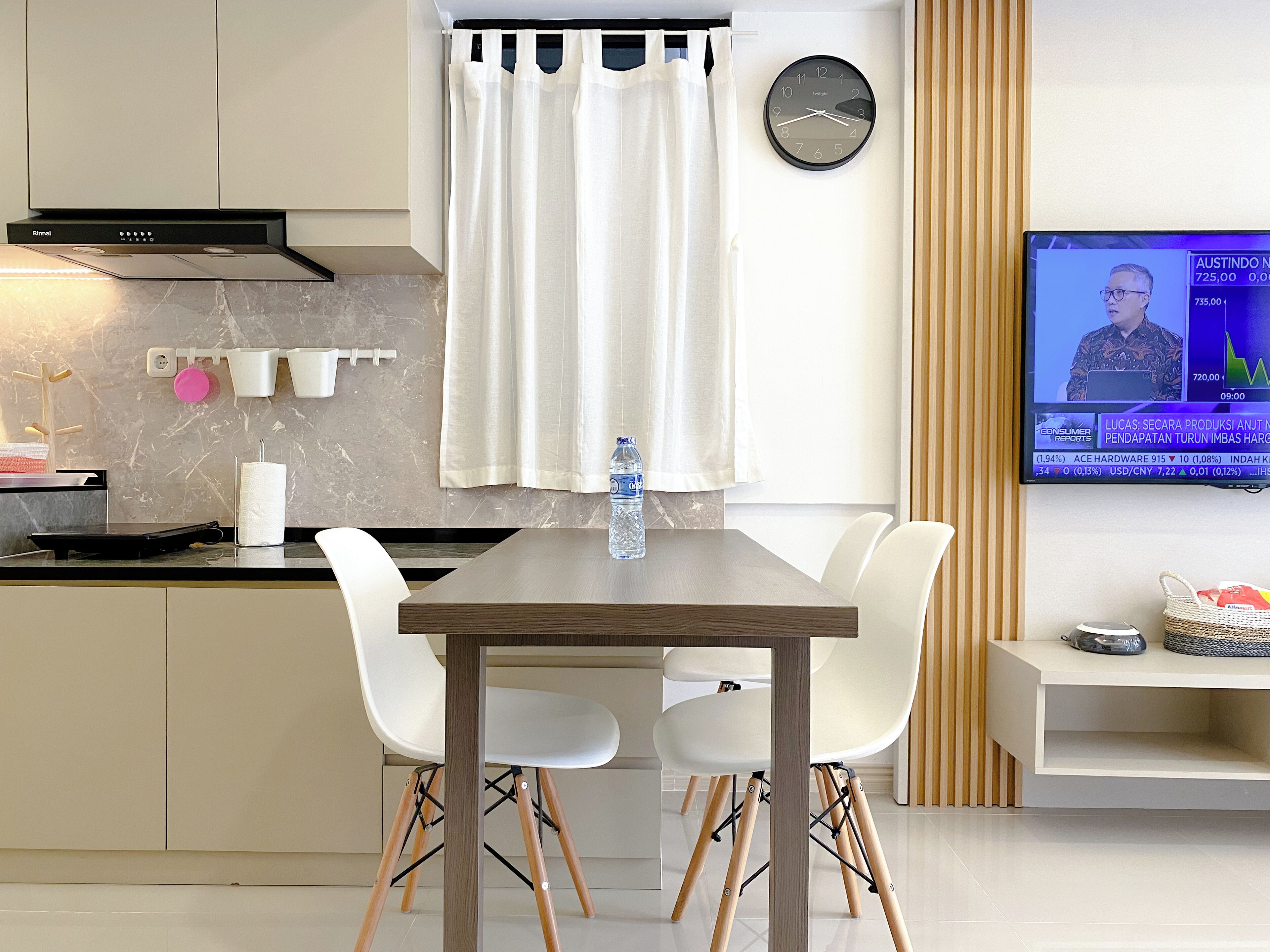 A modern kitchen with a dining area, a TV displaying a news program, and a water bottle on the table.