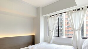 Habitación de hotel con una cama bien hecha, una ventana con cortinas y vistas a edificios.