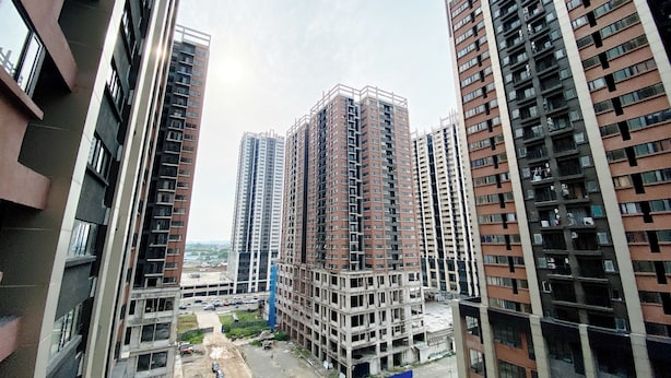 Un edificio residencial de gran altura con varios pisos, ventanas amplias y una obra en construcción al frente.