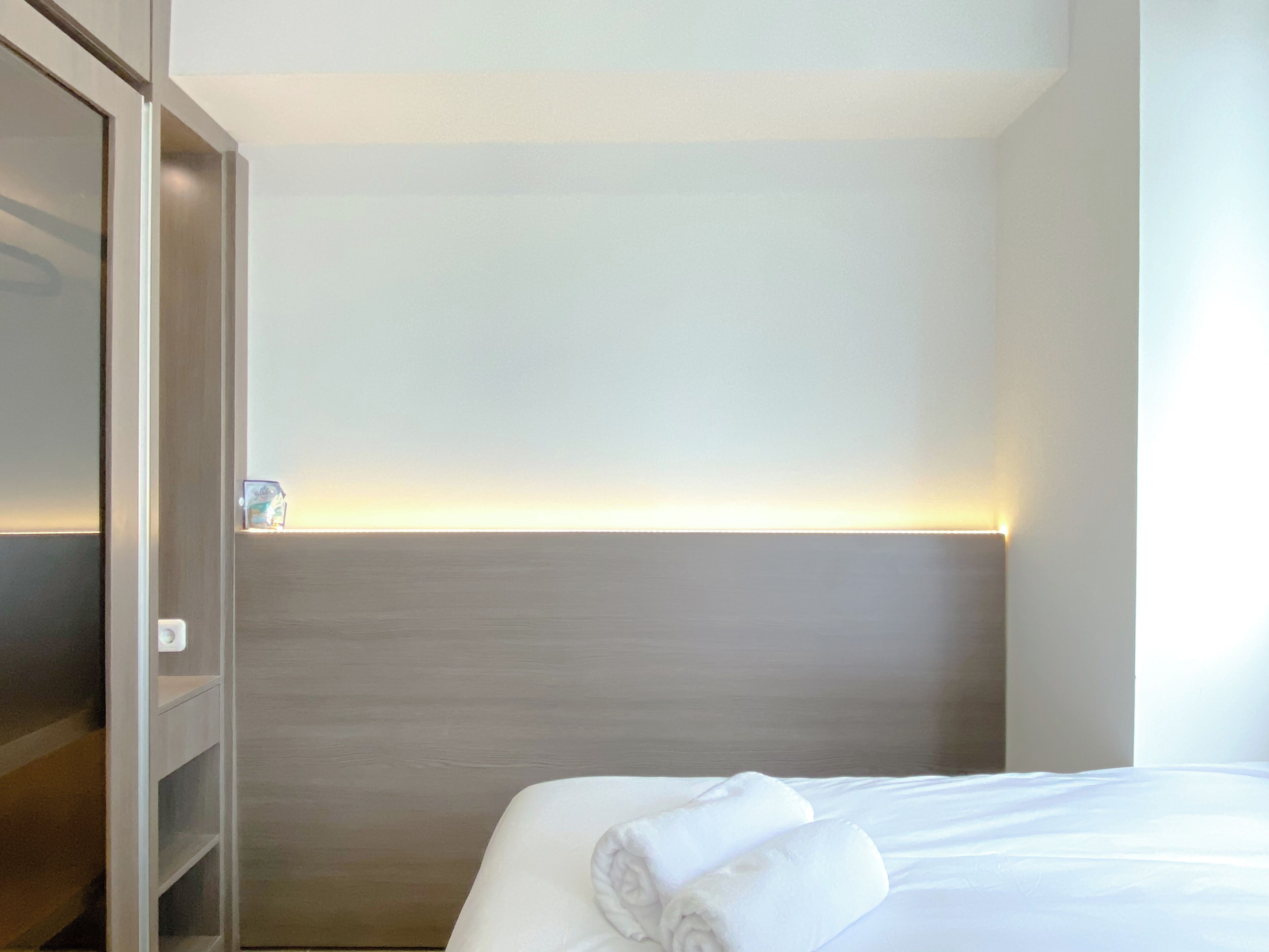 A hotel room with a neatly made bed, a wooden headboard, and a shelf unit.