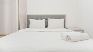 A neatly made bed with white bedding and pillows, a grey headboard, and a white nightstand beside it. - Homey And Modern Design 2Br Apartment At M-Town Residence (Gading Serpong)