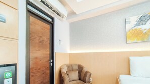 A hotel room with a wooden door, a chair, a bed, and a painting on the wall.