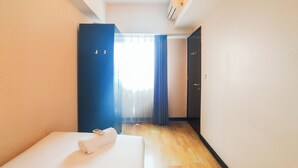 A hotel room with a bed, a blue door, and a window with curtains.