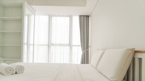Un lit bien fait, avec du linge de lit blanc et des oreillers, une tête de lit en bois et une grande fenêtre ornée de rideaux légers.