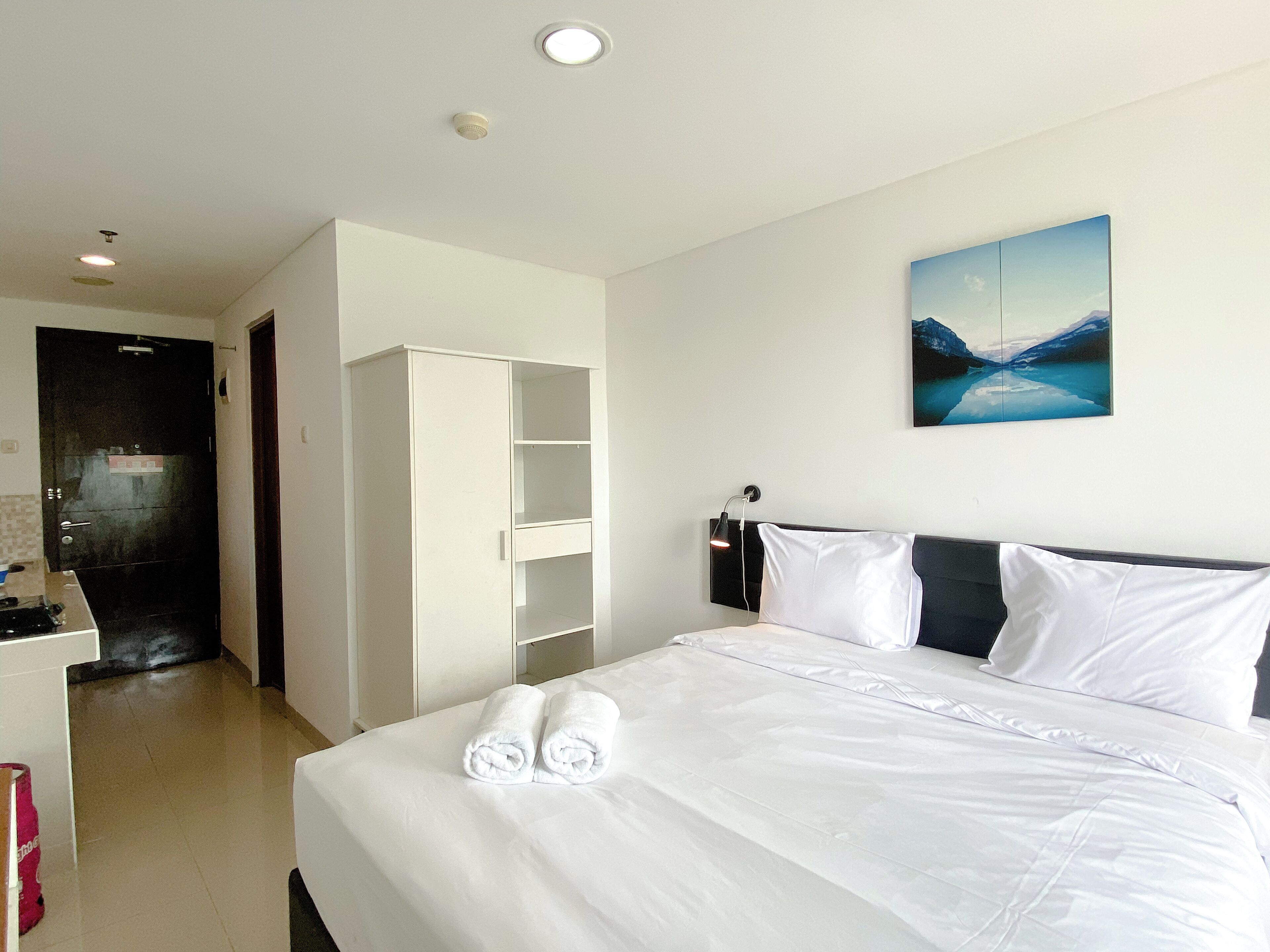 A hotel room with a neatly made bed, a wardrobe, a painting on the wall, and a door to the bathroom.