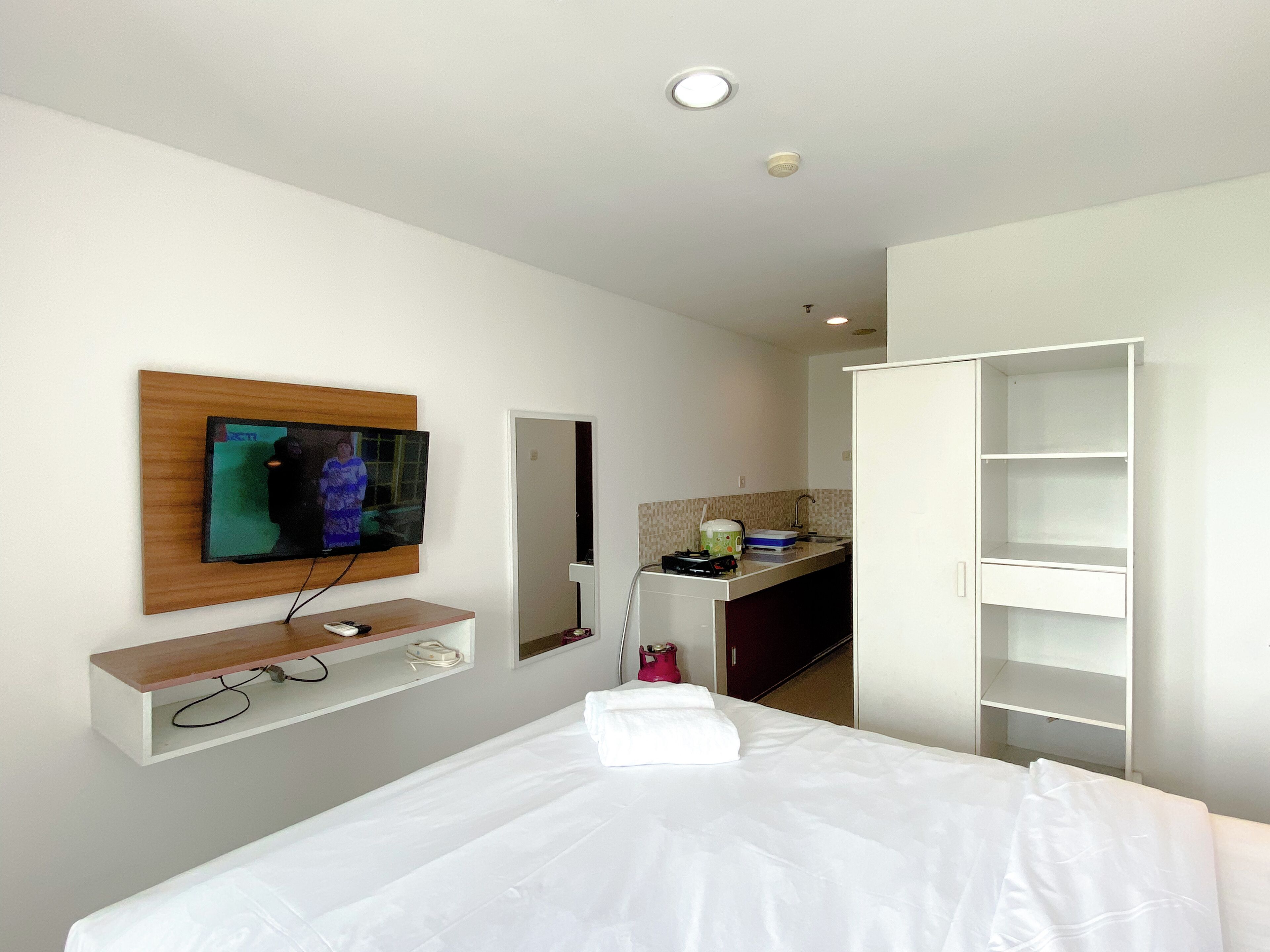 A hotel room with a bed, a TV mounted on a wooden panel, a kitchenette, and a wardrobe.
