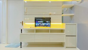 A modern kitchen with a built-in TV displaying a streaming service interface, a white cabinet, and a blue mat on the floor. - Brand New And Modern 2Br At Daan Mogot City Apartment (Jakarta)