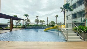 A swimming pool with a yellow slide, surrounded by palm trees and a modern building.