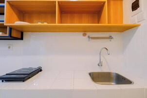 A kitchen with white tiles, a stainless steel sink, a wooden shelf, and a portable induction cooktop.