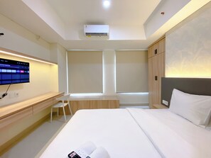 Ein modernes Hotelzimmer mit einem großen Bett, einem Schreibtisch, einem an der Wand montierten Fernseher und einem Fenster mit Jalousien.