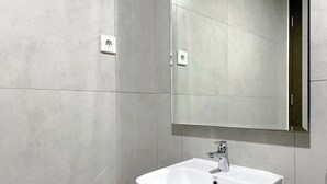 A modern bathroom with a white sink, a mirror, and tiled walls. - Simply Studio Pollux Chadstone Apartment (Cikarang)