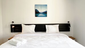 A neatly made bed with white linens, a black headboard, and two white pillows. A folded white towel is placed at the foot of the bed.