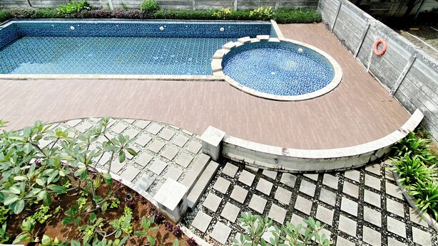 A rectangular swimming pool with a circular hot tub, surrounded by a wooden deck and a brick pathway.
