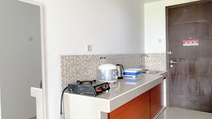 A compact kitchen with a white countertop, a coffee maker, a kettle, and a portable heater.
