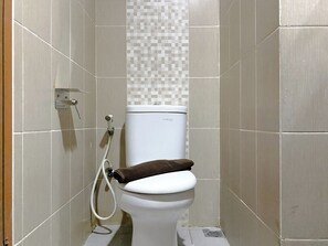 Bathroom features a toilet, toilet paper holder, and a drain.