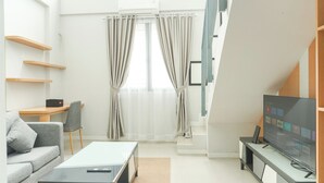 A modern living room with a sofa, coffee table, TV, and a staircase. - Good Deal Studio Loft Mezzanine (No Kitchen) At Kubikahomy Apartment (Pagedangan)