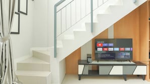 A staircase with a modern design, a flat-screen TV mounted on a wooden cabinet, and a curtain on the left. - Good Deal Studio Loft Mezzanine (No Kitchen) At Kubikahomy Apartment (Pagedangan)