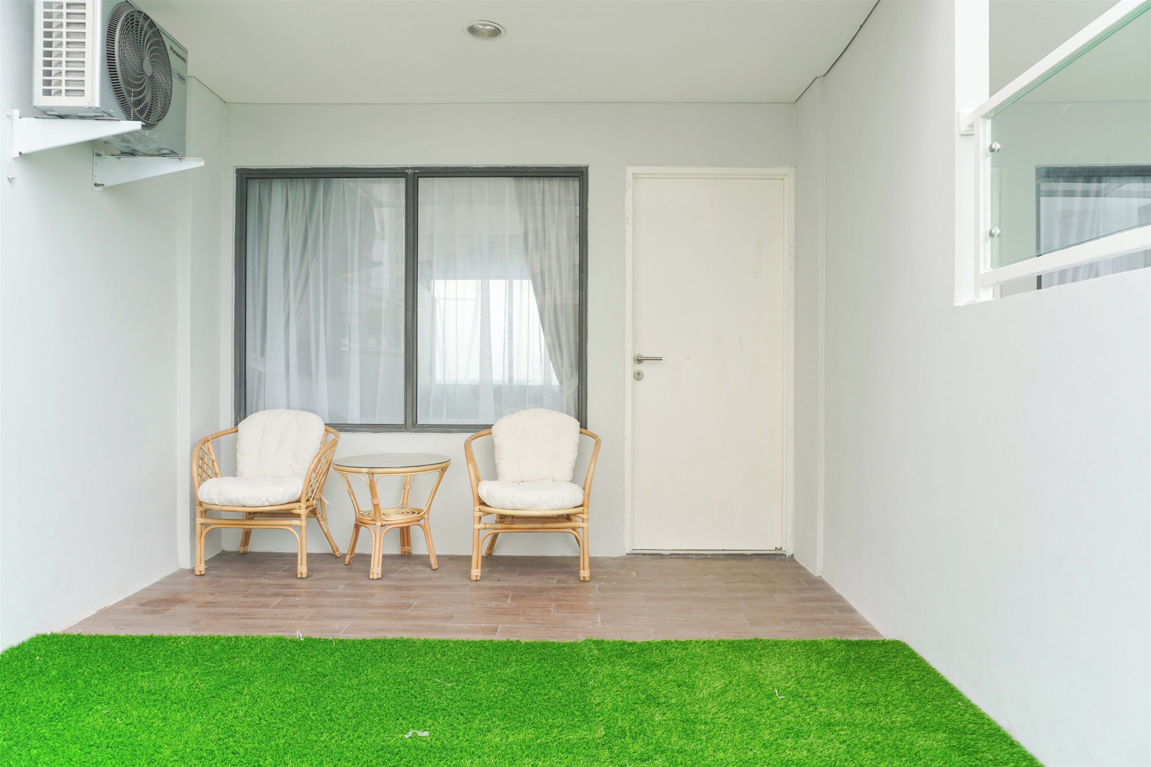A small room with two wicker chairs, a small round table, a white door, and a window with curtains.
