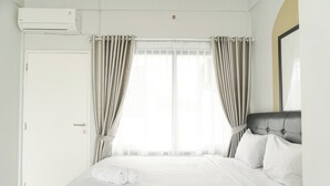 A hotel room with a bed, curtains, an air conditioning unit, and a door. - Good Deal Studio Loft Mezzanine (No Kitchen) At Kubikahomy Apartment (Pagedangan)