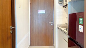 Ein schmaler Flur mit einer Holztür, einem an der Wand montierten Gegensprechanlage und einem Sharp-Kühlschrank.