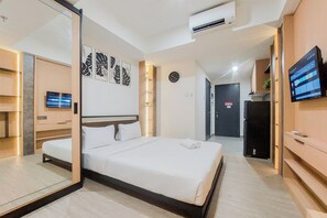 A modern hotel room with a large bed, a flat-screen TV, a wall clock, and a digital display on the wall.