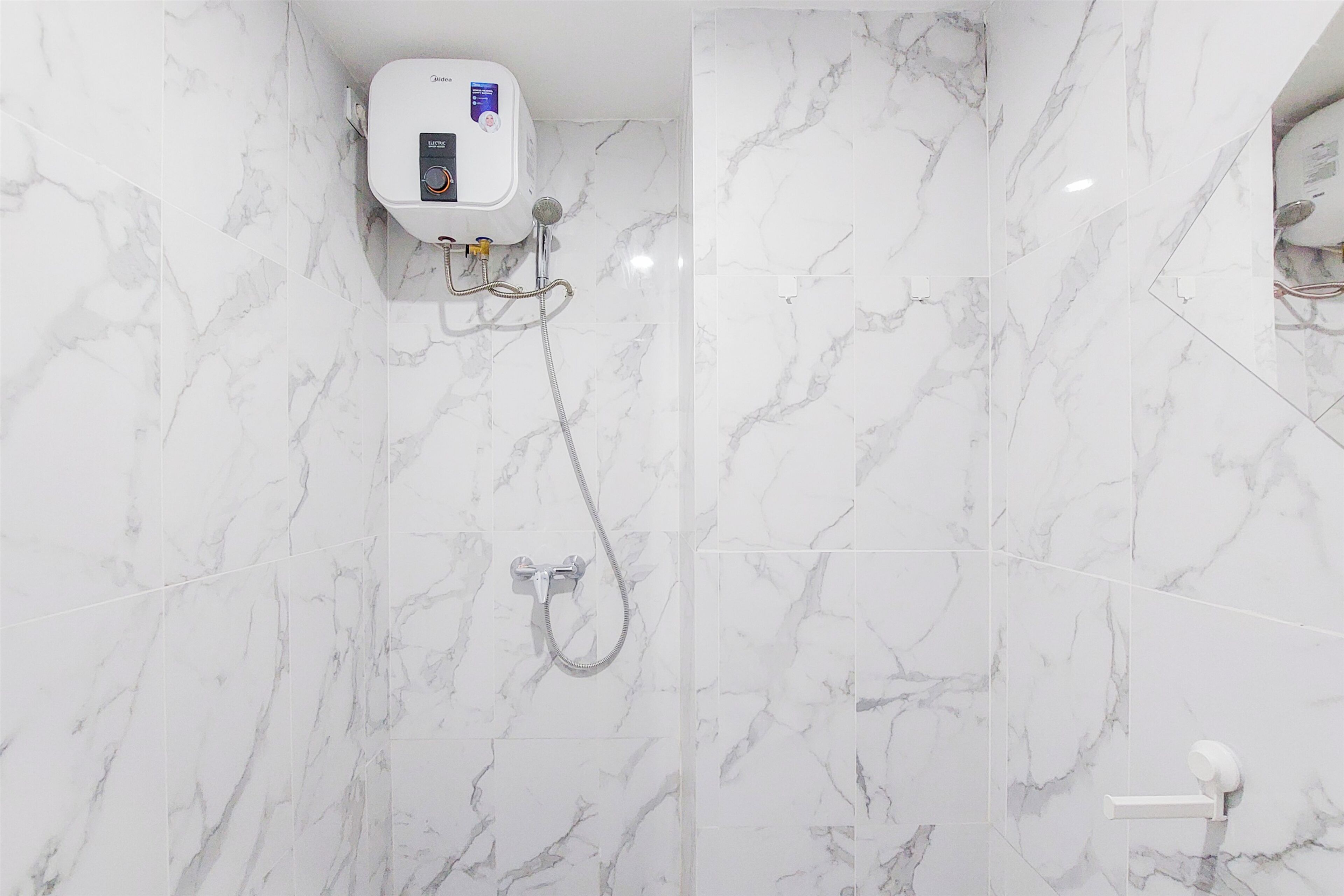 A bathroom with white marble tiles, a handheld showerhead, and a wall-mounted toilet.
