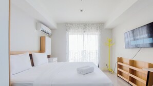 Hotellihuone, jossa on suuri sänky, seinälle asennettu taulutelevisio, puinen yöpöytä ja ikkuna, jossa on läpikuultavat verhot.