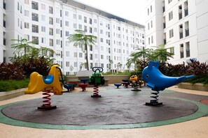 A playground with swings and a slide, surrounded by a building with multiple floors and balconies. - Best Choice And Comfort Living 2Br Bassura City Apartment (Jakarta)