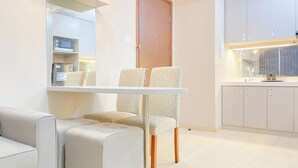 A modern kitchen with white cabinets, a microwave, and a sink. There is a dining table with two chairs. - Good Choice And Homey 2Br Signature Park Grande Apartment (Jakarta)